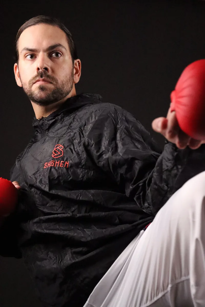 Atleta a executar um pontapé com o corta-vento preto Shomen e luvas vermelhas