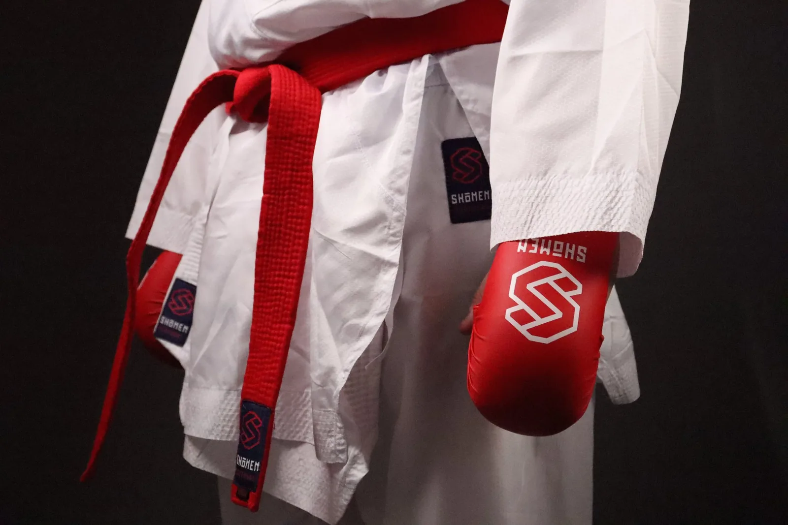Pormenor de um kimono de kumite branco Shomen com cinto vermelho e luva vermelha